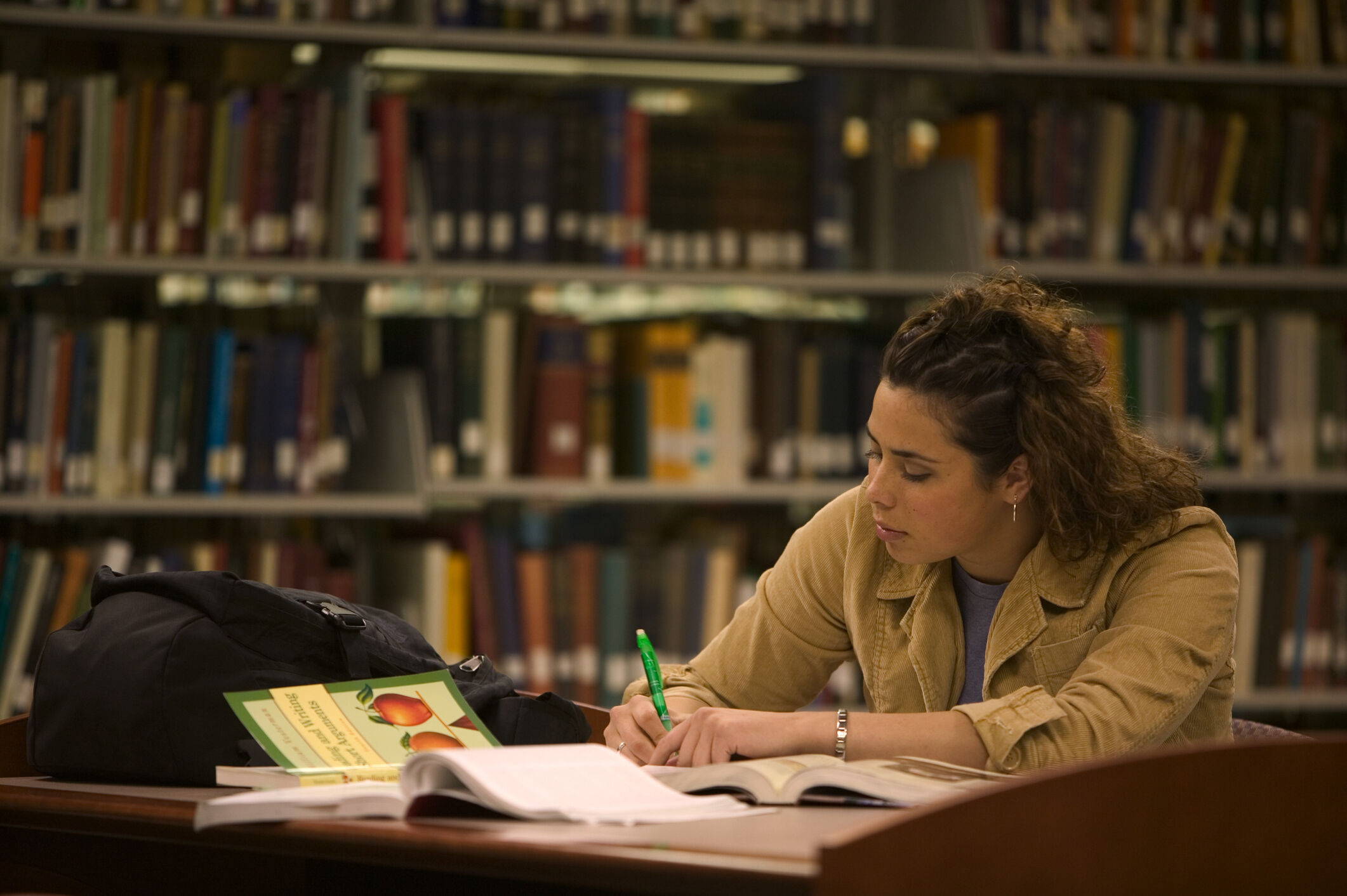 A teacher candidate sits at a desk in a library. She takes notes in a notebook while studying for her Praxis exam.